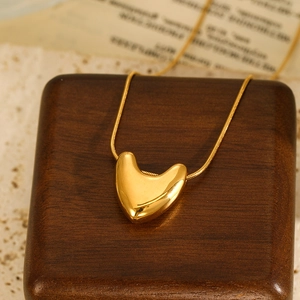 Macro detail of a polished gold heart pendant with a sleek snake chain on a wooden base