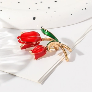 Elegant gold tulip brooch with red and green enamel on a ceramic tray backdrop
