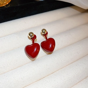 Close-up of red heart earrings with gold beads on beige velvet display tray