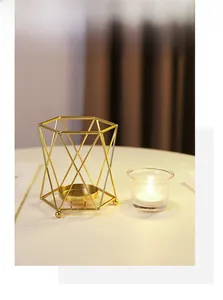Close-up of golden geometric metal candle holder with a small glass cup and lit candle