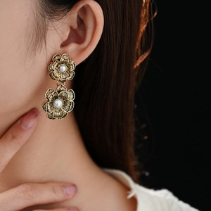 Close-up of vintage golden flower earrings with white pearl centers worn by model