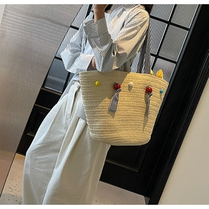 Detail of beige straw tote with colorful pom-poms and tassels for beach vacation