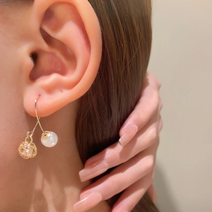 Detail van gouden holle metalen bolletjes oorbellen met witte parels en haken voor dames