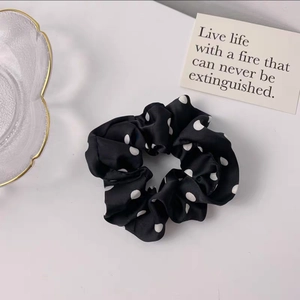 Polka dot silk scrunchie with white dots on black fabric displayed on a white surface