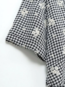 Détail de la broderie florale sur le tissu de la chemise vichy noir et blanc