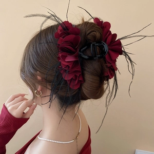 Detail view of burgundy fabric flower hair claw with feathers worn by a model