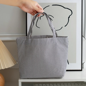 Minimalist black and white striped tote bag held by hand in a cozy lifestyle setting