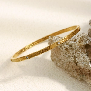 Macro detail of 18K gold plated hammered texture bangle with small round diamonds on coral stone