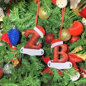 Close-up of red glitter Christmas letter ornament with DIY banner on a pine tree