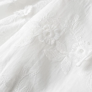 Close-up of intricate 3D floral embroidery on white cotton fabric for two-piece sets