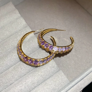 Detail of gold C-shaped earrings with purple and white zircon in a grey velvet box