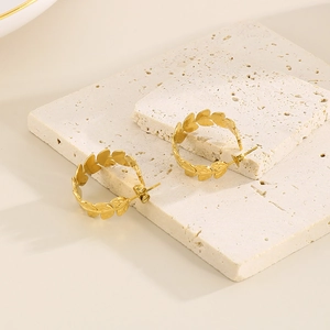 Detail of golden leaf C-shaped stainless steel earrings on a beige stone display