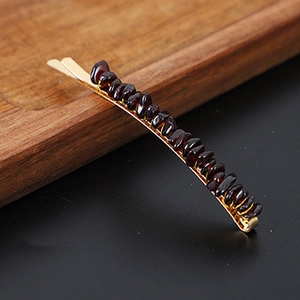 Macro shot of gold hair clip with natural reddish-brown garnet stone beads on wood