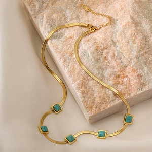 Bohemian gold snake chain necklace with five square turquoise stones on stone backdrop