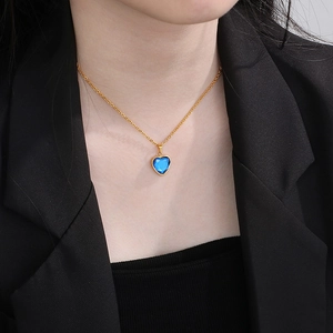 Nahaufnahme einer eleganten Goldkette mit blauem Herzanhänger an einem Model