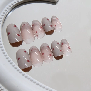 French bow and red star design on oval press-on nails displayed on a vintage mirror