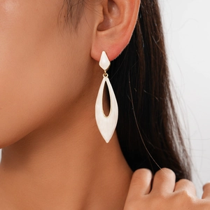 Close-up of white enamel teardrop earrings with gold trim worn by a model