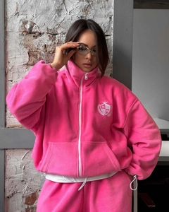 Détail d'une veste polaire rose avec fermeture éclair blanche et écusson logo couronne