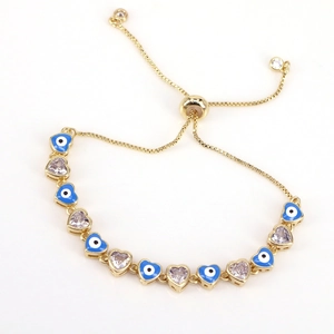 Detail eines goldenen Armbands mit blauem Evil-Eye-Herz und lila Zirkon-Elementen