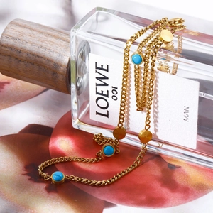 Close-up of a gold turquoise necklace chain wrapped around a luxury perfume bottle