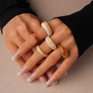 Close-up of set of acrylic resin geometric rings in amber and cream worn by a model
