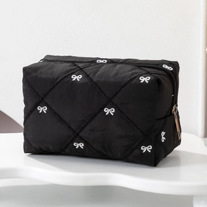 Detail of black quilted makeup bag featuring white bow embroidery and gold zipper