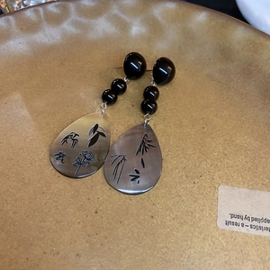 Macro detail of retro water-drop earrings with etched rose and bird motifs in ceramic tray
