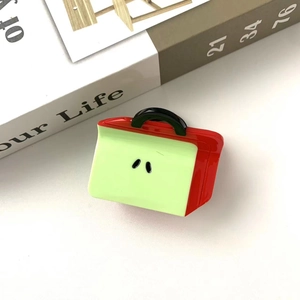 Detail view of a cute apple-shaped hair claw clip in red and light green acrylic