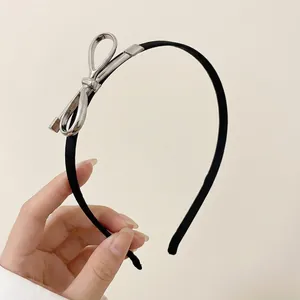 Detail of thin black headband with silver metallic bow buckle accent held by hand