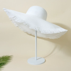 Detail of a white woven straw sun hat with frayed edges on a stand with green leaves