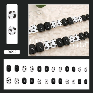 Detail view of square cow print and glossy black press-on nails set in 24 pieces