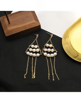 Macro shot of gold tassel pearl earrings with triangular frame and cascading fine chains