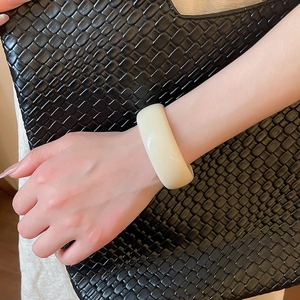 Gros plan du large bracelet jonc en acrylique crème sur poignet avec fond noir texturé