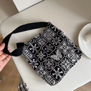 Detail of elegant black canvas shoulder bag with white butterfly embroidery and floral patterns