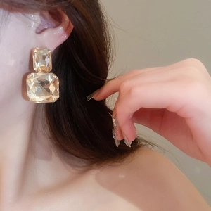 Macro shot of large golden square stud earring with faceted crystals worn by a model