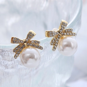 Détail macro d'une boucle d'oreille nœud doré avec zircons et perle blanche élégante
