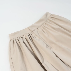 Detail of beige pleated high-waisted shorts featuring elegant fabric folds and textures