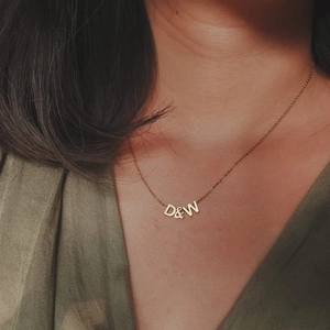 Close-up of a delicate gold necklace with D and W letter pendants on a model's neck