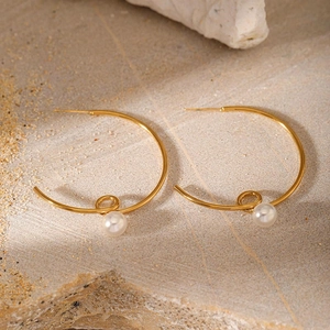 Detail of a C-shaped gold earring with a white pearl on a natural stone background