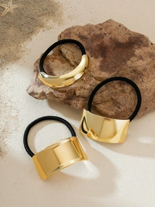 Close-up of black elastic hair ties with gold geometric metal buckles on a beach setting