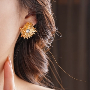 Macro detail of gold flower stud earring with shimmering center zircon on a model