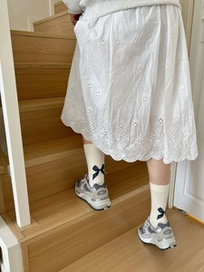 Detail of white hollow embroidered skirt and cream bow mid-calf socks on a model