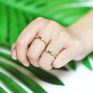 Close-up van gouden ringen met rechthoekige rode en groene zirkoonstenen op de hand
