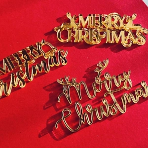 Three-piece set of gold acrylic Merry Christmas cake toppers on a festive red background