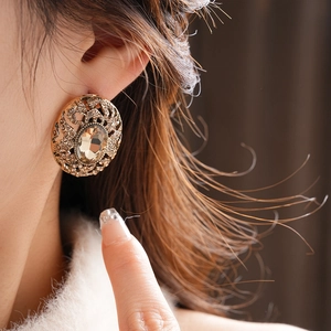 Close-up of vintage oval gold earring with amber crystal and hollow metal patterns