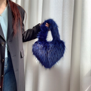 Close-up of heart-shaped dark blue faux fur handbag held by a model in a black coat