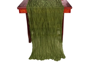Detail shot of green wrinkled table runner with soft gauze texture on a wooden table