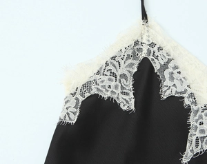 Detailed close-up of white eyelash lace trim on black satin camisole top