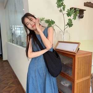 Détail d'une robe longue en jean bleu sans manches et d'un sac à bandoulière noir plissé chic