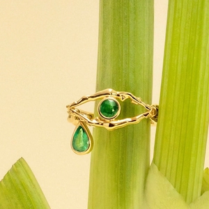 Macro shot of gold-plated evil eye ring with emerald drop stone on a green stem